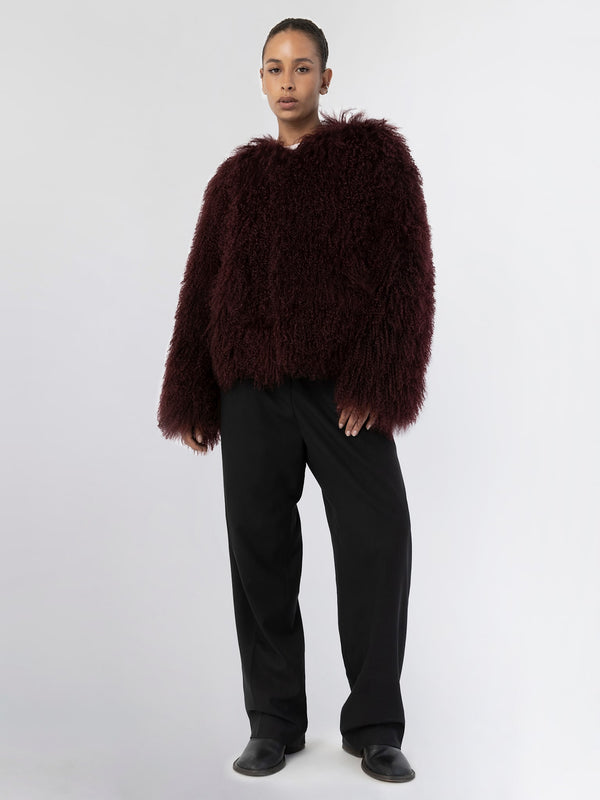 A model wears a plush, burgundy faux fur jacket paired with black wide-leg trousers, showcasing MEOTINE's cozy style.
