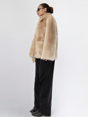 A model showcases a luxurious beige faux fur coat by MEOTINE, paired with sleek black trousers and stylish sunglasses.