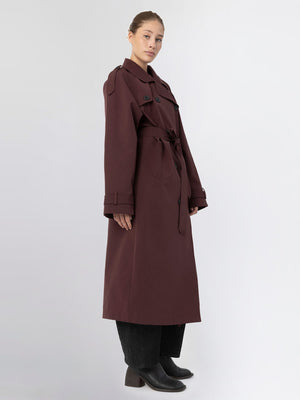 A model showcases a long burgundy trench coat with a belt, featuring a classic collar and button details, by MEOTINE.