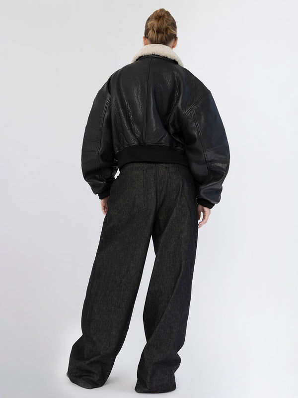A model showcases a stylish black leather bomber jacket with a cozy fur collar, paired with wide-leg dark denim pants by MEOTINE.