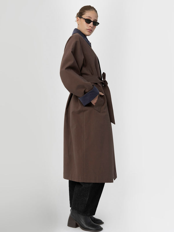 A model showcases a stylish brown coat with a belt, paired with dark jeans and sunglasses, embodying MEOTINE's chic aesthetic.