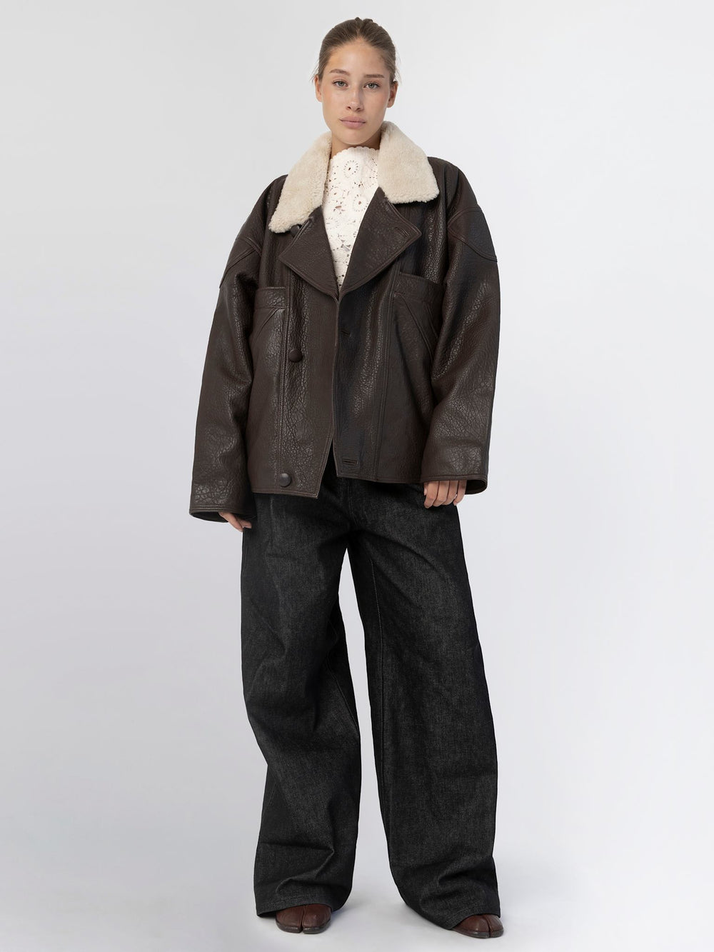 A model showcases a stylish brown leather jacket with a plush collar, paired with wide-leg dark jeans, embodying MEOTINE's chic aesthetic.