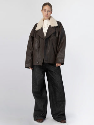 A model showcases a stylish brown leather jacket with a plush collar, paired with wide-leg dark jeans, embodying MEOTINE's chic aesthetic.