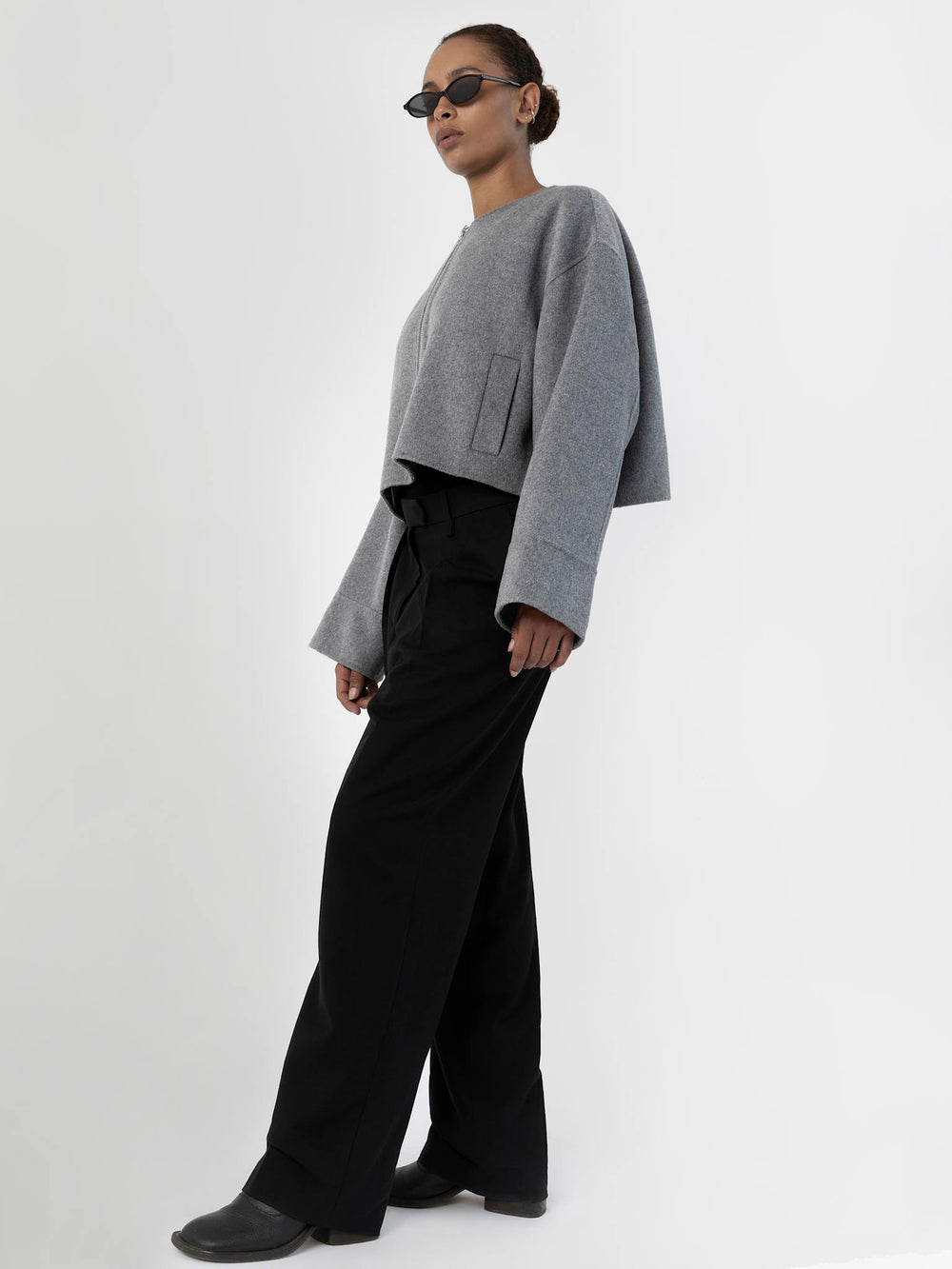 A model wears a cropped gray jacket with a zip front and wide sleeves, paired with black trousers and stylish sunglasses. MEOTINE.
