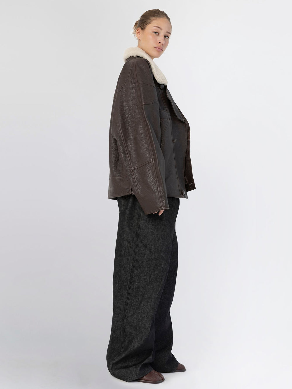 A model showcases a stylish brown leather jacket with a plush collar, paired with wide-leg dark jeans, embodying MEOTINE's chic aesthetic.