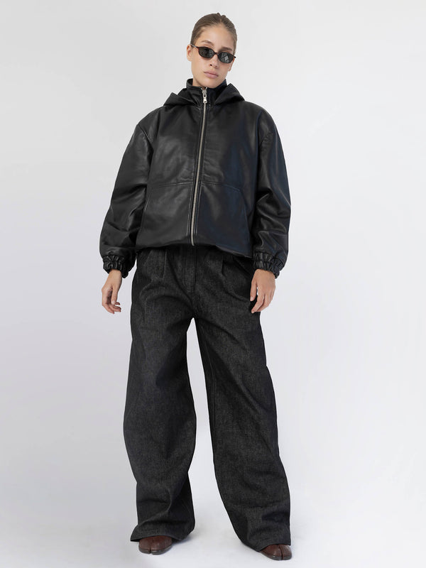 A model showcases a stylish black leather jacket paired with oversized dark denim pants, embodying a chic urban look by MEOTINE.
