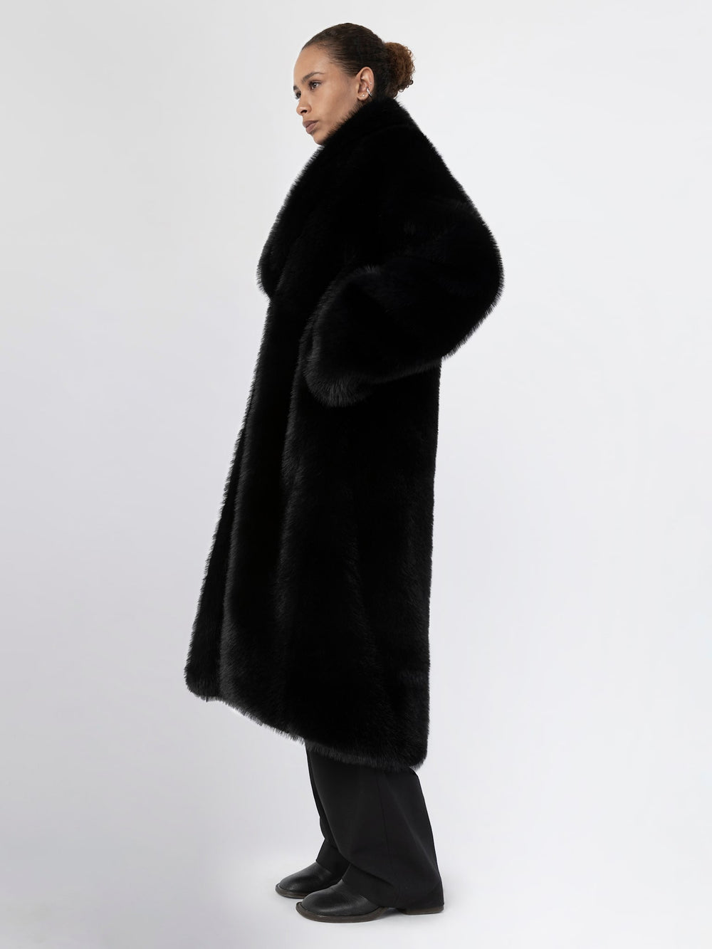A model wears a luxurious black faux fur coat by MEOTINE, featuring a wide collar and a relaxed fit, perfect for stylish warmth.