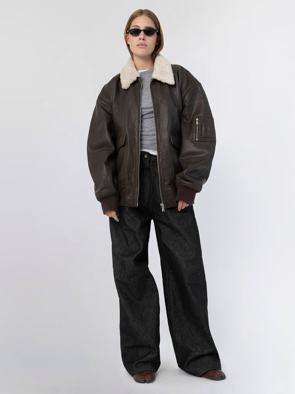 A model showcases a stylish brown leather jacket with a shearling collar, paired with oversized black pants, embodying MEOTINE's chic aesthetic.