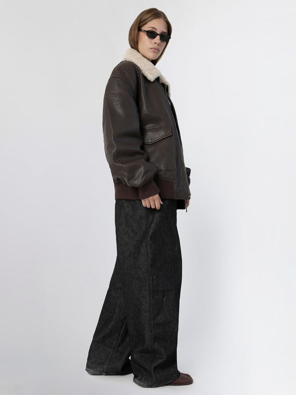 A model showcases a brown leather jacket with a shearling collar, paired with wide-leg dark jeans, embodying MEOTINE's stylish aesthetic.