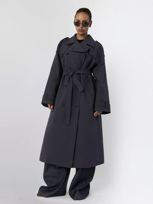 A model showcases a stylish dark trench coat with a belt, paired with wide-leg jeans and sunglasses, representing MEOTINE's chic aesthetic.