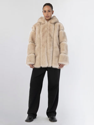 A model wears a plush beige MEOTINE fur coat with a hood, paired with black wide-leg trousers against a neutral background.