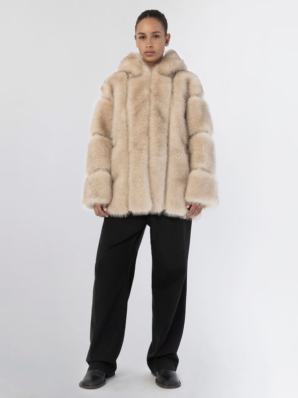 A model wears a plush beige MEOTINE fur coat with a hood, paired with black wide-leg trousers against a neutral background.
