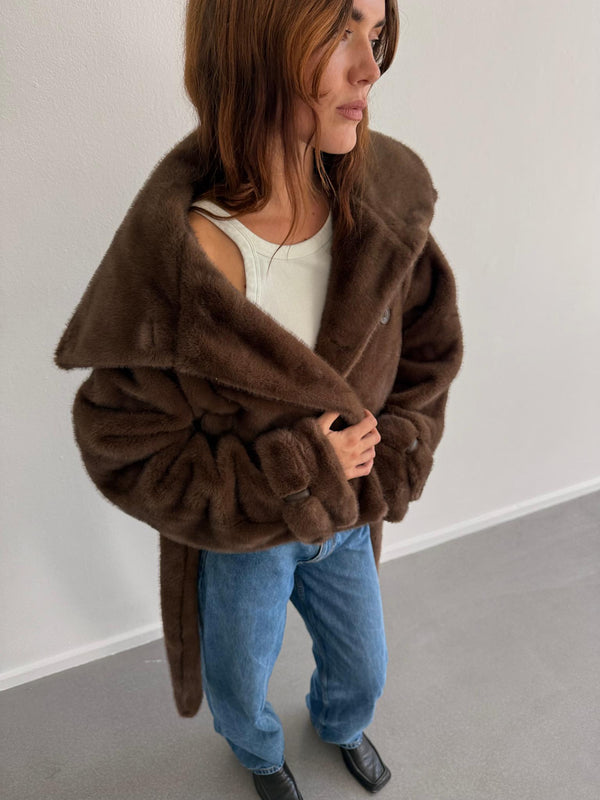 A model wearing a cozy brown faux fur coat from MEOTINE, paired with a simple white top and blue jeans, exuding casual elegance.