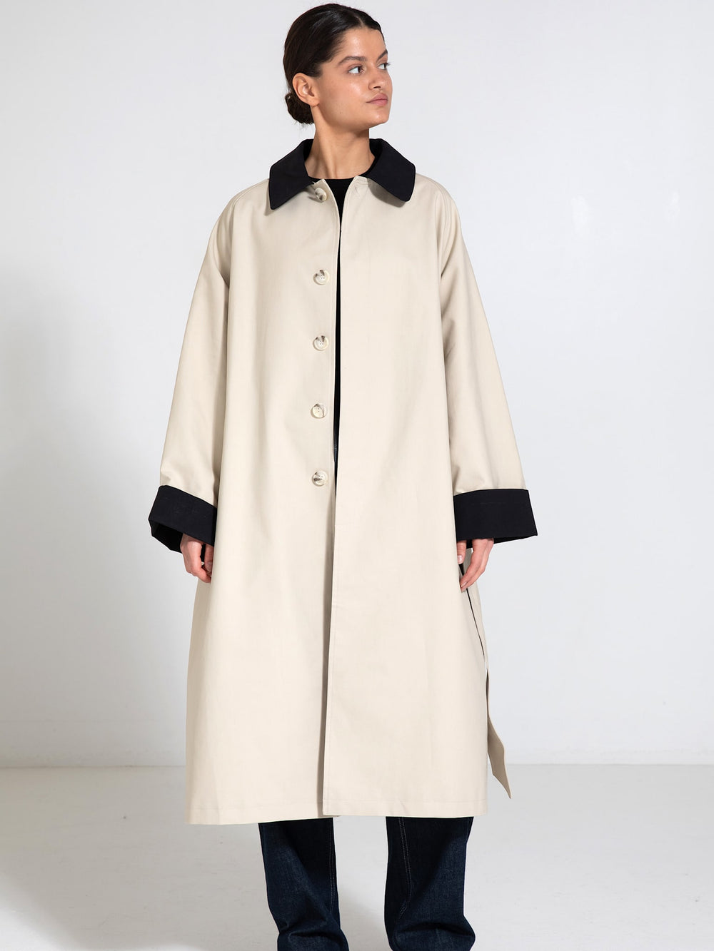 A model wearing a beige trench coat with a black collar and cuffs, showcasing a stylish and modern design by MEOTINE.