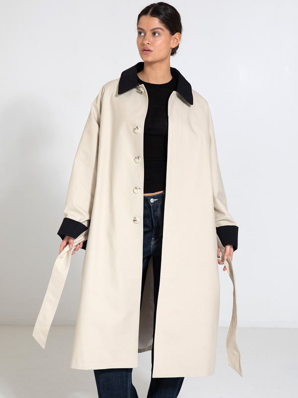 A model wears a stylish beige MEOTINE coat with a black collar, paired with a black top and jeans, showcasing a modern look.