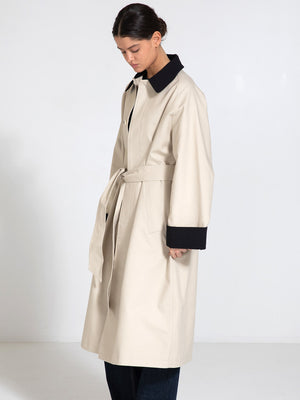 A model wearing a beige trench coat with a black collar and cuffs, showcasing a stylish and modern design by MEOTINE.