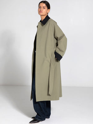 A model showcases a stylish MEOTINE oversized coat in olive green, paired with dark jeans and a black top, set against a minimalist backdrop.
