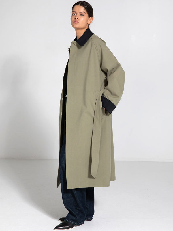 A model showcases a stylish MEOTINE oversized coat in olive green, paired with dark jeans and a black top, set against a minimalist backdrop.