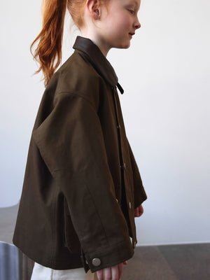 A girl in a stylish brown MEOTINE jacket, showcasing a modern design with a collar, set against a minimalist background.