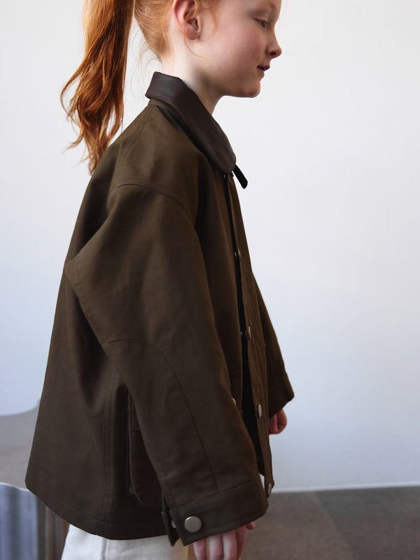 A girl in a stylish brown MEOTINE jacket, showcasing a modern design with a collar, set against a minimalist background.