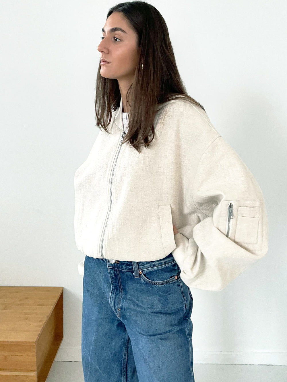 A model showcases a stylish beige oversized bomber jacket by MEOTINE, paired with a simple white tee and denim jeans.