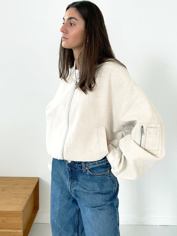A model showcases a cream-colored MEOTINE zip-up jacket paired with high-waisted blue jeans, exuding a casual, stylish vibe.