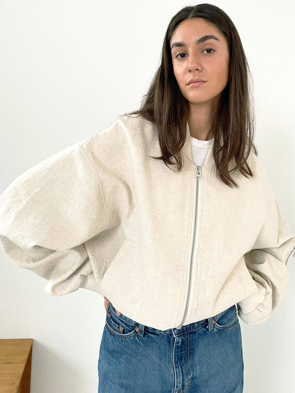 A model wearing a cream-colored oversized jacket with a zip, paired with a white t-shirt and blue jeans, showcasing MEOTINE style.