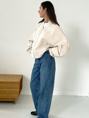 A model showcases a stylish oversized cream bomber jacket paired with loose blue jeans, embodying a relaxed, modern look. MEOTINE.