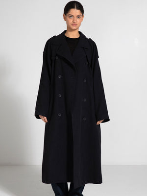 A model wears a long, dark trench coat with a relaxed fit and double-breasted buttons, showcasing MEOTINE's stylish design.