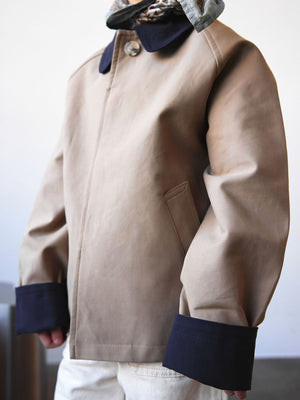 A child wearing a stylish beige MEOTINE jacket with a dark collar and cuffs, showcasing a modern and trendy design.