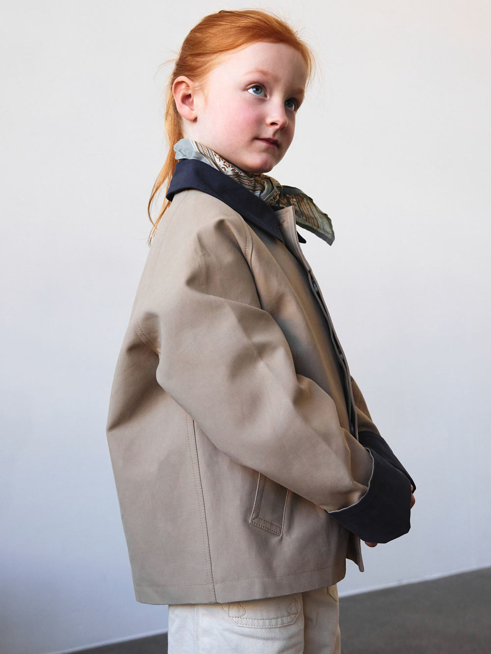 A child models a stylish beige jacket with navy cuffs and a scarf, paired with wide-leg white pants, showcasing MEOTINE's trendy design.