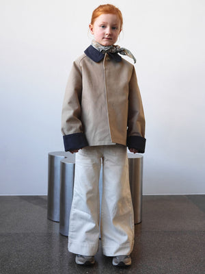 A child models a stylish beige jacket with navy cuffs and a scarf, paired with wide-leg white pants, showcasing MEOTINE's trendy design.