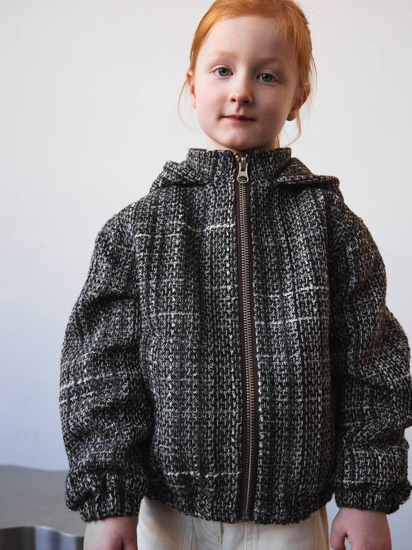 A young girl models a cozy, textured black and white jacket with a zip, showcasing MEOTINE's stylish winter collection.