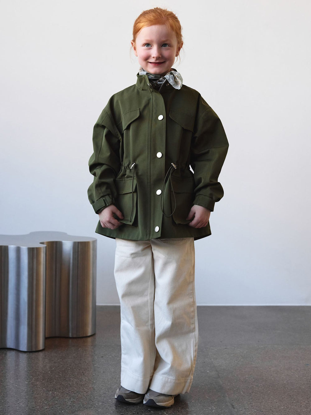 A young girl models a stylish green MEOTINE jacket with a cinched waist and snap buttons, showcasing a modern, trendy design.