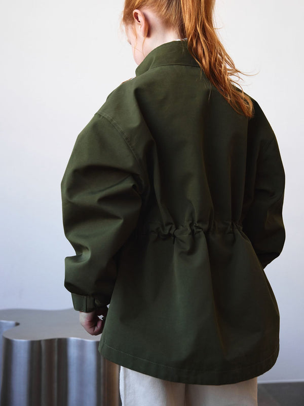 A child wearing a green MEOTINE jacket with a cinched waist, showcasing a relaxed fit and stylish design from the back.