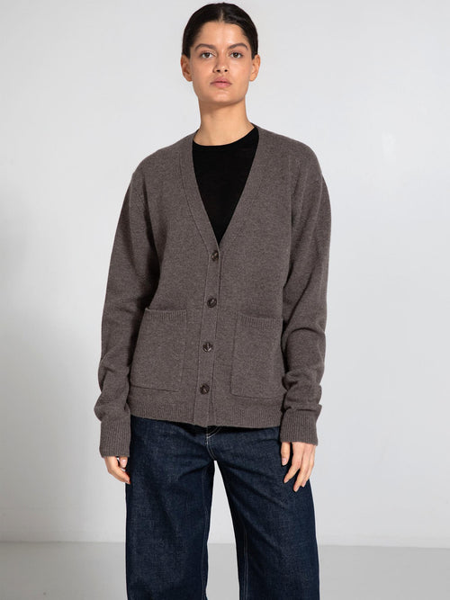 A model wears a cozy, brown cardigan with a V-neck and button closure, featuring two front pockets, by MEOTINE.