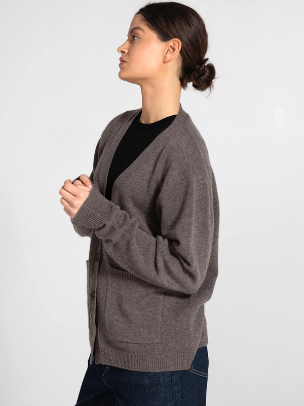 A woman models a cozy, brown cardigan with buttons and pockets, styled with a black top and casual jeans, by MEOTINE.