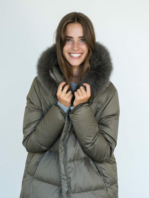 A smiling woman in a cozy olive green puffer jacket with a fur-lined hood, showcasing MEOTINE's stylish winter outerwear.
