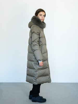 A model showcases a long, olive green puffer coat with a fur-lined hood, embodying the stylish warmth of MEOTINE.