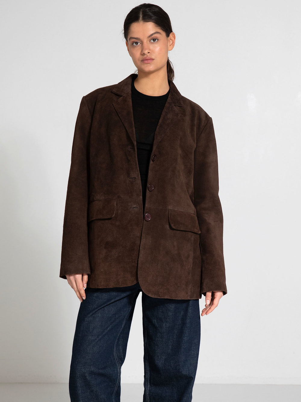 A model showcases a brown suede blazer with a relaxed fit, featuring a button closure and two front pockets, by MEOTINE.
