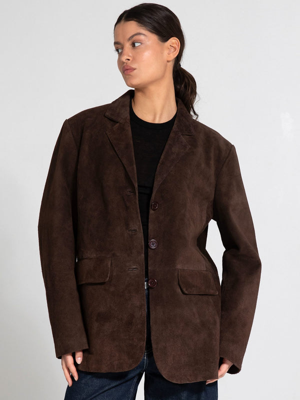 A model showcases a brown suede blazer with a relaxed fit, featuring a button closure and two front pockets, by MEOTINE.
