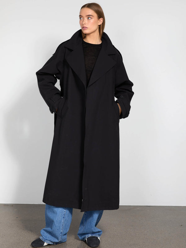 A model wearing a long black coat with a wide collar, paired with blue jeans, showcasing MEOTINE's stylish outerwear.
