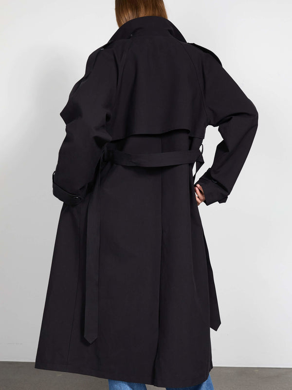 A model showcases a stylish black trench coat from MEOTINE, featuring a belted waist and a classic silhouette, viewed from the back.