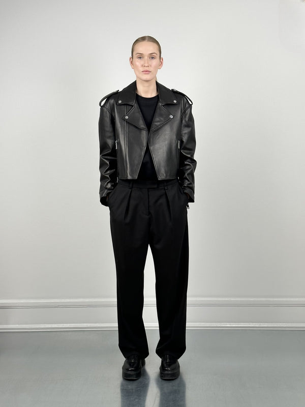 A model showcases a stylish black leather jacket paired with loose black trousers, embodying a chic, modern look by MEOTINE.