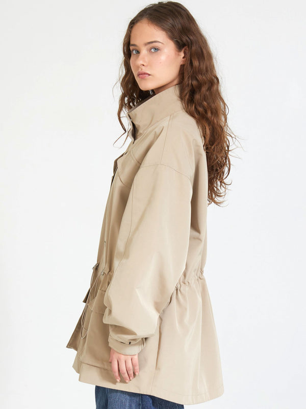 A model wearing a beige MEOTINE jacket with a cinched waist, showcasing a relaxed fit and stylish design.