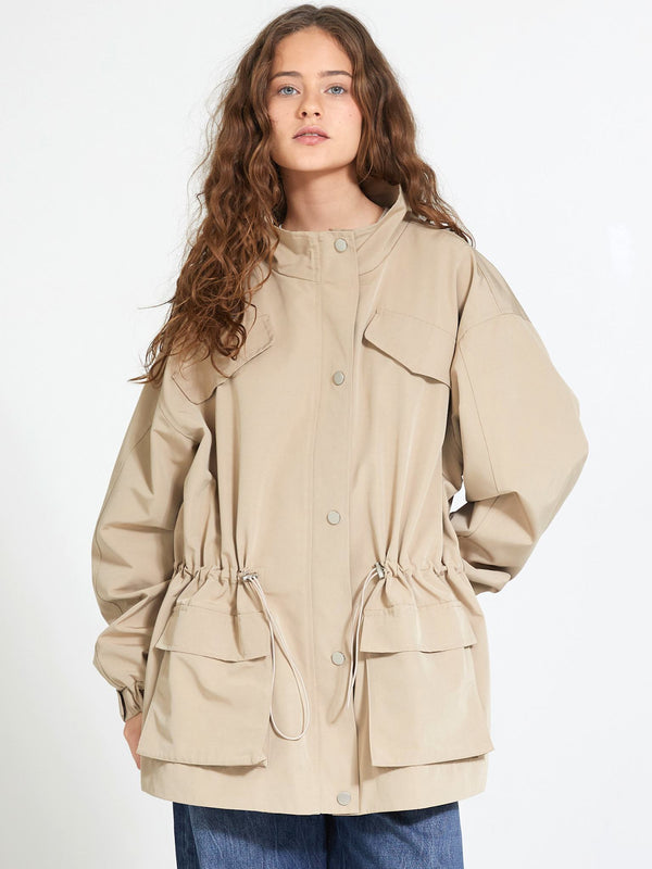 A model wearing a beige MEOTINE jacket with a cinched waist and large pockets, styled with loose blue jeans.