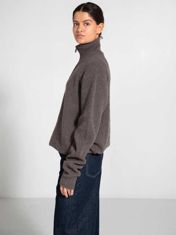 A model wearing a cozy, taupe MEOTINE sweater with a high collar and long sleeves, paired with dark denim jeans.