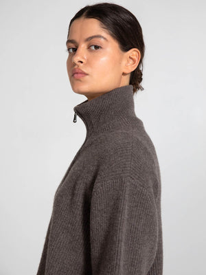 A model showcases a stylish, high-neck sweater in a warm brown tone, embodying the cozy elegance of MEOTINE.