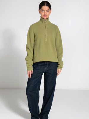 A model wears a light green, ribbed zip-up sweater paired with dark blue jeans, showcasing a casual and stylish look by MEOTINE.
