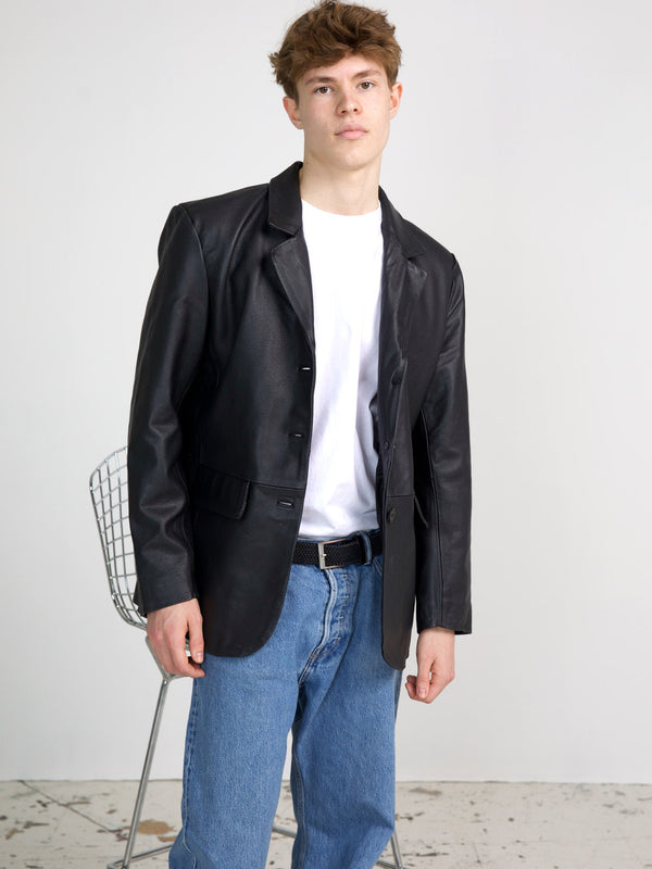 A young man poses in a stylish black leather blazer over a white t-shirt, paired with blue jeans, showcasing MEOTINE's modern design.